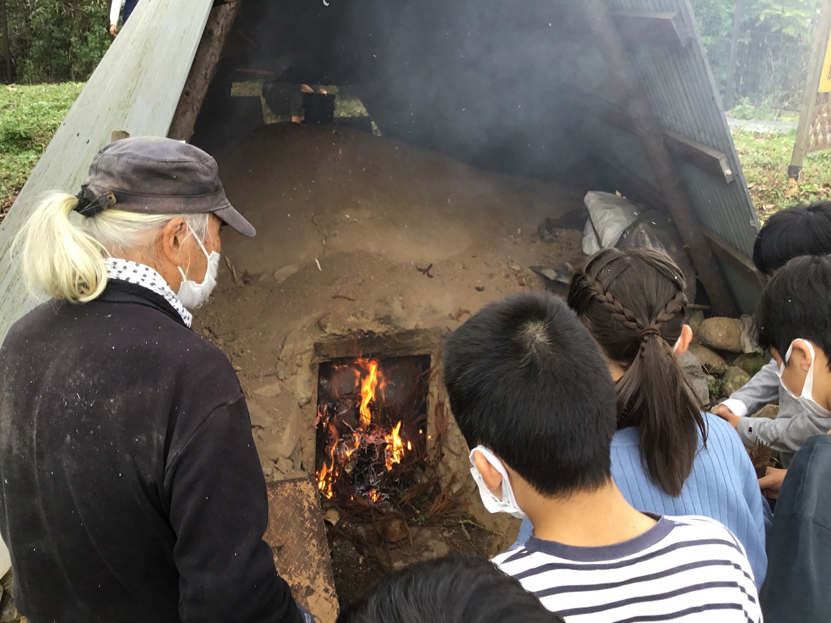 炭焼きを見守る地域の人と児童